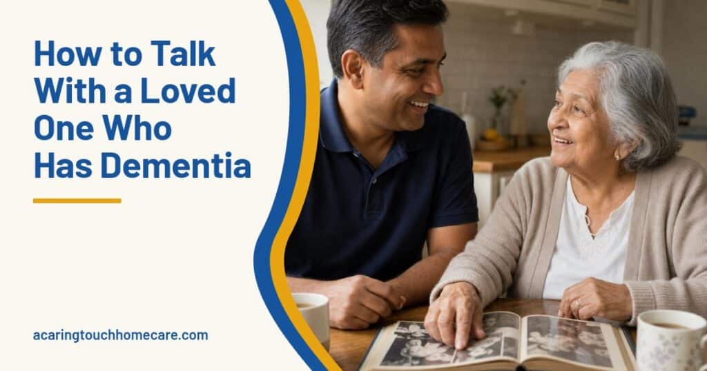 A caregiver and an older woman smile over a photo album at a sunny kitchen table, chatting comfortably.